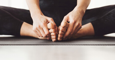 Cropped of woman is seated on a yoga mat in a cross-legged position, gently pulling their toes forward as part of a stretching routine, panorama