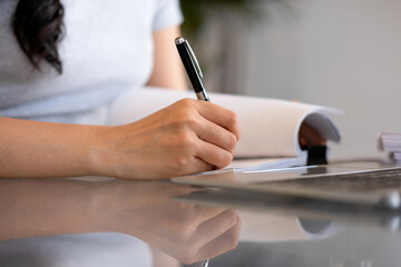 Fototapeta premium Young woman engages in note-taking at workspace.
