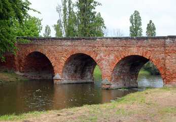 medieval bridge made of red bricks with three perfect arches over a canal with water