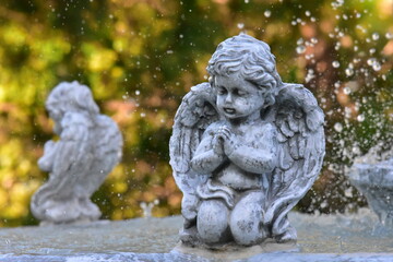 Statues of an angel, a child, and a person in a garden with stone, marble, and ancient architecture, reflecting religious and cultural themes