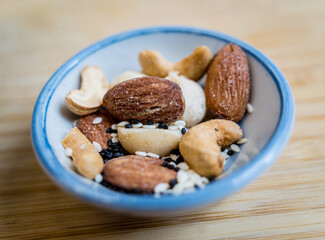 A bowl filled with assorted nuts and seeds is placed on a rustic wooden table