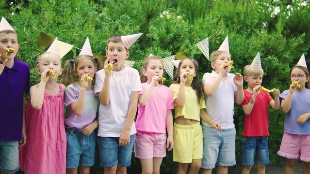 At outdoor birthday party children in party hats laughing and blowing a whistle, having joyful and festive atmosphere