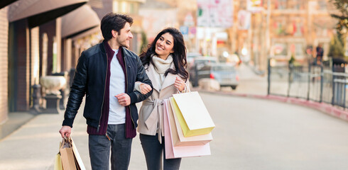 A man and a woman are strolling down a city street carrying shopping bags.