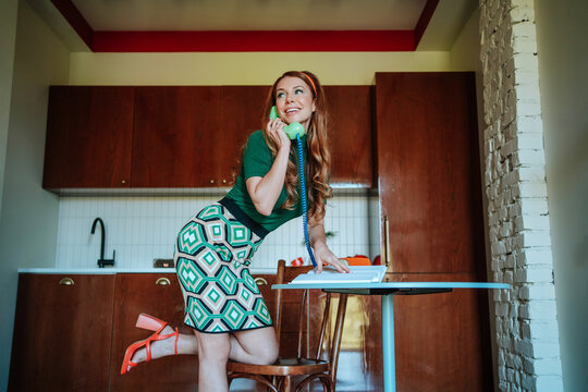 Playful 1950s housewife chatting on phone while ironing