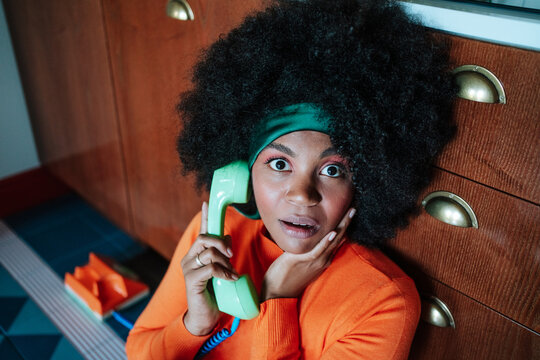 Surprised Black African american woman talking on retro phone in vintage style kitchen