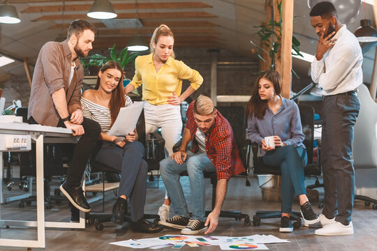 A diverse team discusses and reviews project materials spread on the floor in a modern office, engaging in a collaborative brainstorming session.