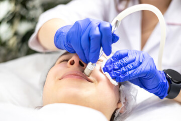 Naklejka premium Close up under view, cosmetician makes micro needling treatment to the smiling patient using derma pen and wearing blue medical gloves.