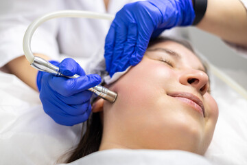 A professional dermatologist wearing medical gloves performs a microdermabrasion procedure on a...