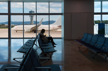 Silhouette of young woman working on laptop and waiting for flight in the Airport - El Prat-Barcelona airport. This airport was inaugurated in 1963 - Barcelona, Spain 