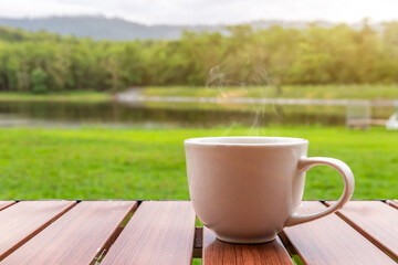 A white cup of hot espresso coffee mugs placed on a wooden floor and natural pool with sunlight background,coffee morning