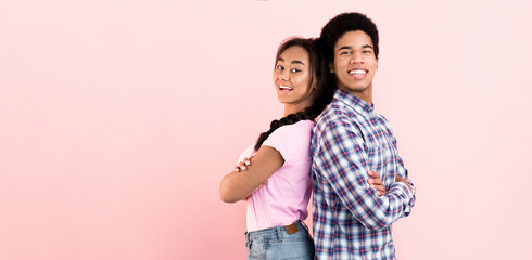 A young black couple stands against a vibrant pink backdrop, striking a pose for the camera. Both...
