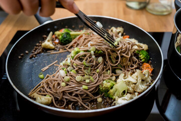 Chef at the kitchen preparing japanese buckwheat pasta with lentils