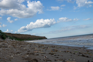 A landscape painting rather than a photograph, it depicts a sandy beach with a calm sea in the background. The surface of the water is smooth and the horizon separates the sea from the light blue sky.