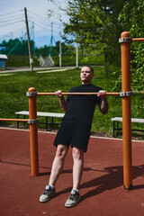 Caucasian male athlete doing pull-ups on the horizontal bar outdoors in a summer park