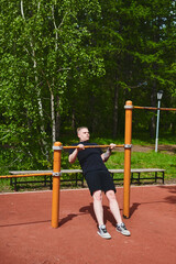 Obraz premium Caucasian male athlete doing pull-ups on the horizontal bar outdoors in a summer park