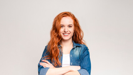 Fototapeta premium A red-haired woman is striking a pose for a photograph. She stands confidently, looking directly at the camera with a captivating gaze