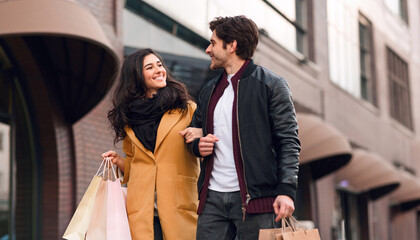 Fototapeta premium A man and woman are walking down a busy street, holding shopping bags in their hands.