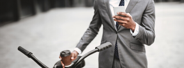 A business professional is using his phone while seated on a bicycle in the city. The scene is...
