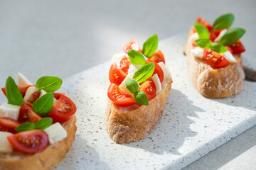 Bruschetta with cherry tomatoes, mozzarella cheese and basil in sun rays on marble board. Traditional Italian appetizer, snack or antipasto. Vegetarian food. Healthy eating. Mediterranean food.