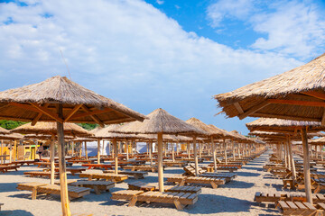 Sunshades with thatched roof and sun loungers on the beach by the sea.