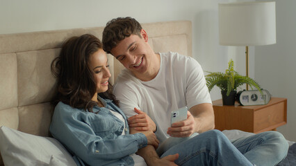 Couple together mobile phone smartphone telephone man woman female male laughing talking gadget bedroom bed home web online digital guy girl showing technology cyberspace typing screen wife husband