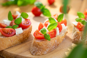 Caprese bruschetta with tomatoes, mozzarella cheese and basil in sun rays on wooden board. Traditional Italian appetizer, snack or antipasto. Vegetarian food. Healthy eating. Mediterranean food.