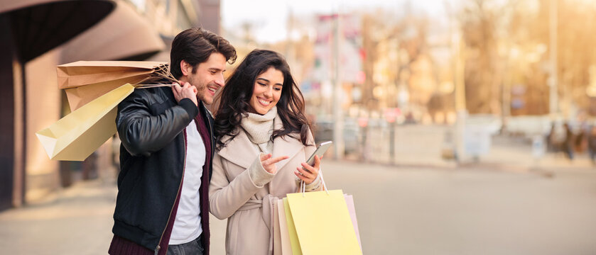 Order taxi online. Couple using smartphone after shopping in modern boutiques outdoors