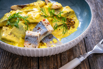 Marinated herring fillets in mustard sauce with dill and lettuce on wooden table
