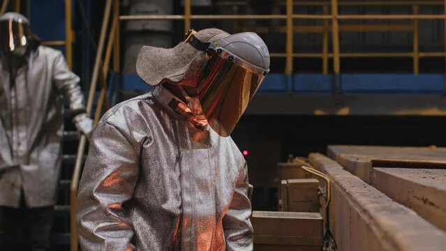 A man in a fireproof suit stands in the smelting shop of a metallurgical plant.