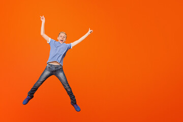 Adorable happy boy jumping and raising his hands up in air. orange studio background