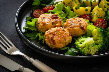 Cooked meatballs, boiled broccoli, boiled potatoes and fresh vegetables on wooden table
