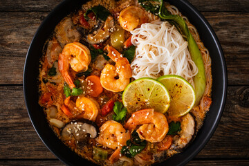 Tom Yam Kung soup - Thai soup with shrimps and rice noodles served in black bowl with chopsticks on wooden table
