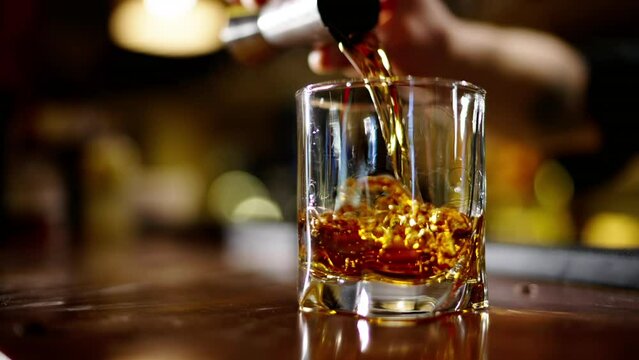 A professional bartender is preparing an alcoholic cocktail with ice cubes to customers at the bar or disco club. Close up of a professional bartender is mixing an alcoholic cocktail with professional