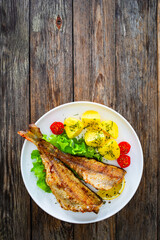 Fried sea bass served on lettuce with boiled potatoes and  lemon on white plate on wooden table
