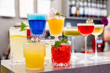 A vibrant collection of colorful cocktails on a bar counter, showcasing an array of flavors and garnishes, ideal for advertising or menu design
