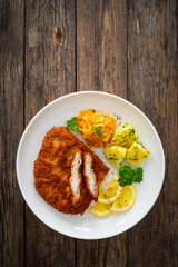 Crispy breaded fried pork chop, boiled potatoes and sauerkraut salad on wooden table
