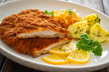 Crispy breaded fried pork chop, boiled potatoes and sauerkraut salad on wooden table
