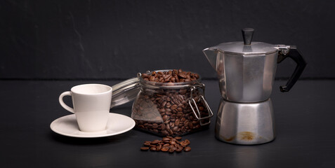 Espresso cup, moka pot and a jar of coffee beans on a black slate surface. Coffee concept.