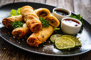 Spring rolls and sauces on wooden table
