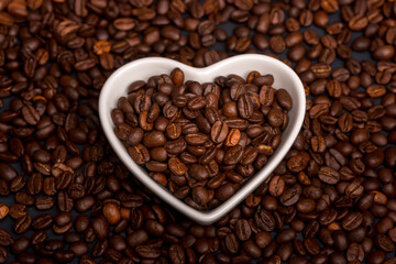 Heart shaped dish with coffee beans and texture background of beans. Love coffee concept.