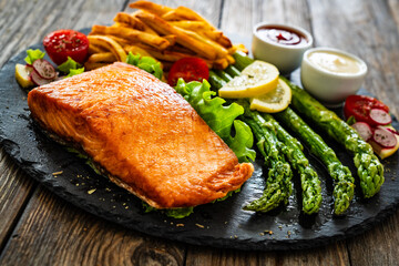 Fried salmon steak with French fries and mayonnaise served on wooden table
