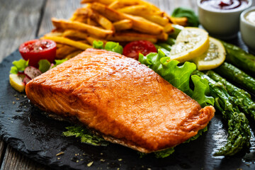 Fried salmon steak with French fries and mayonnaise served on wooden table
