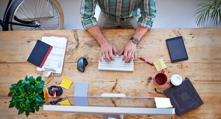 Typing, creative person and hands from above for productivity, communication and review in modern office. Desk, wireless keyboard and computer on table for email, design and networking on internet