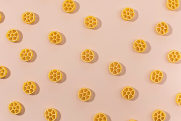 Uncooked rotelle pasta scattered on a pink background, Italian cuisine