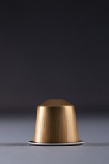 A close-up of a gold coffee capsule on a gradient background, showcasing its sleek, modern design.