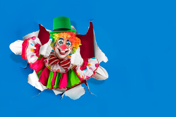 Funny clown thumbs up looking through the ripped paper hole, man entertainer as Joker in a suit and...