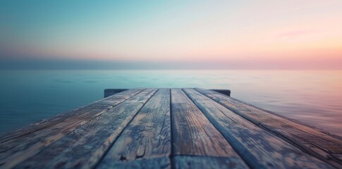 Obraz premium Wooden dock extending into tranquil sea under pastel sunset sky.