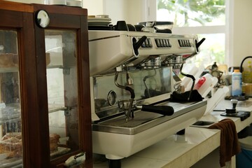 Fototapeta premium Cozy cafe scene featuring a professional espresso machine and a pastry display case. The natural light enhances the warm, inviting atmosphere, ideal for coffee enthusiasts and cafe lovers.