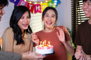 friend birthday cake. young asian woman blows out a birthday cake that friends brought for a birthday party. celebrating Birthday party. Group of friends smiling enjoying party