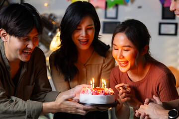 friend birthday cake. young asian woman blows out a birthday cake that friends brought for a birthday party. celebrating Birthday party. Group of friends smiling enjoying party